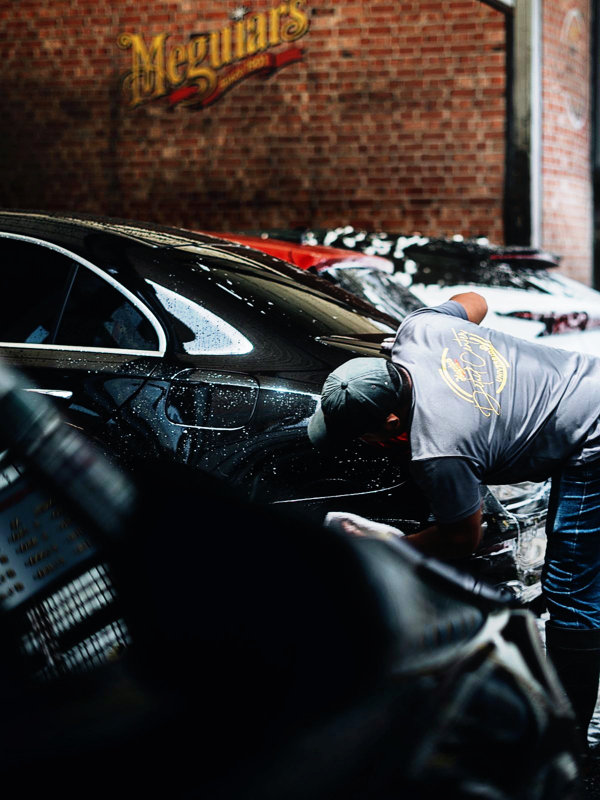 Detallador puliendo un auto negro frente al logo de Meguiar’s